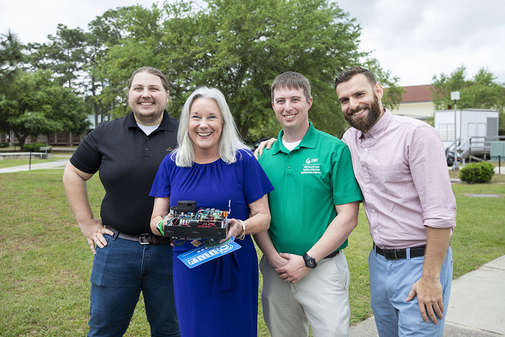 UWF President Martha Saunders poses with the university's Robotics Team and their prize-winning creation on the Cannon Green.