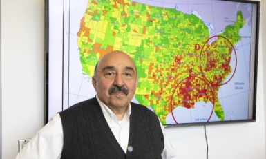 Dr. Raid Amin, a distinguished university professor in the Department of Mathematics and Statistics, stands before a map where his research has identified high rates of breast cancer death in America.