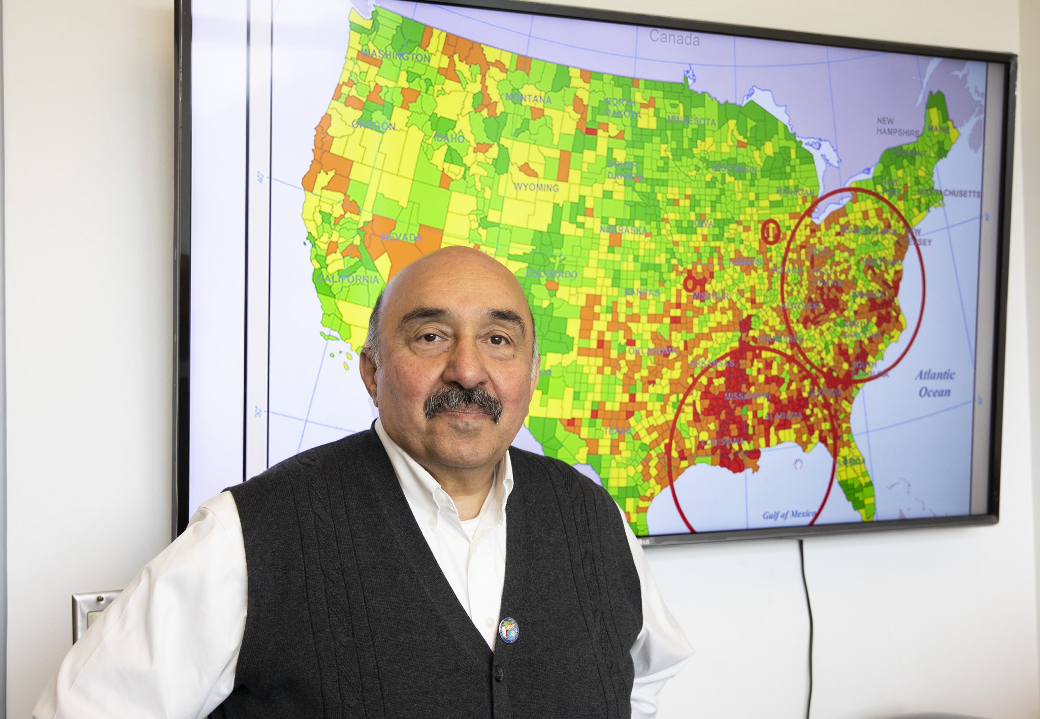 Dr. Raid Amin, a distinguished university professor in the Department of Mathematics and Statistics, stands before a map where his research has identified high rates of breast cancer death in America.