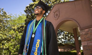 UWF graduate poses in front of the archway on the Pensacola campus.