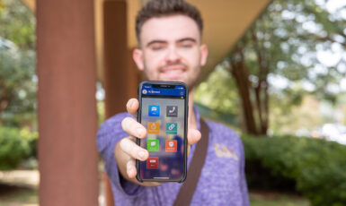 Student holding a mobile phone pointing at the camera with the UWF Gaudian app displayed on the screen.