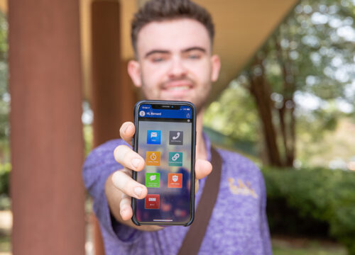 Student holding a mobile phone pointing at the camera with the UWF Gaudian app displayed on the screen.