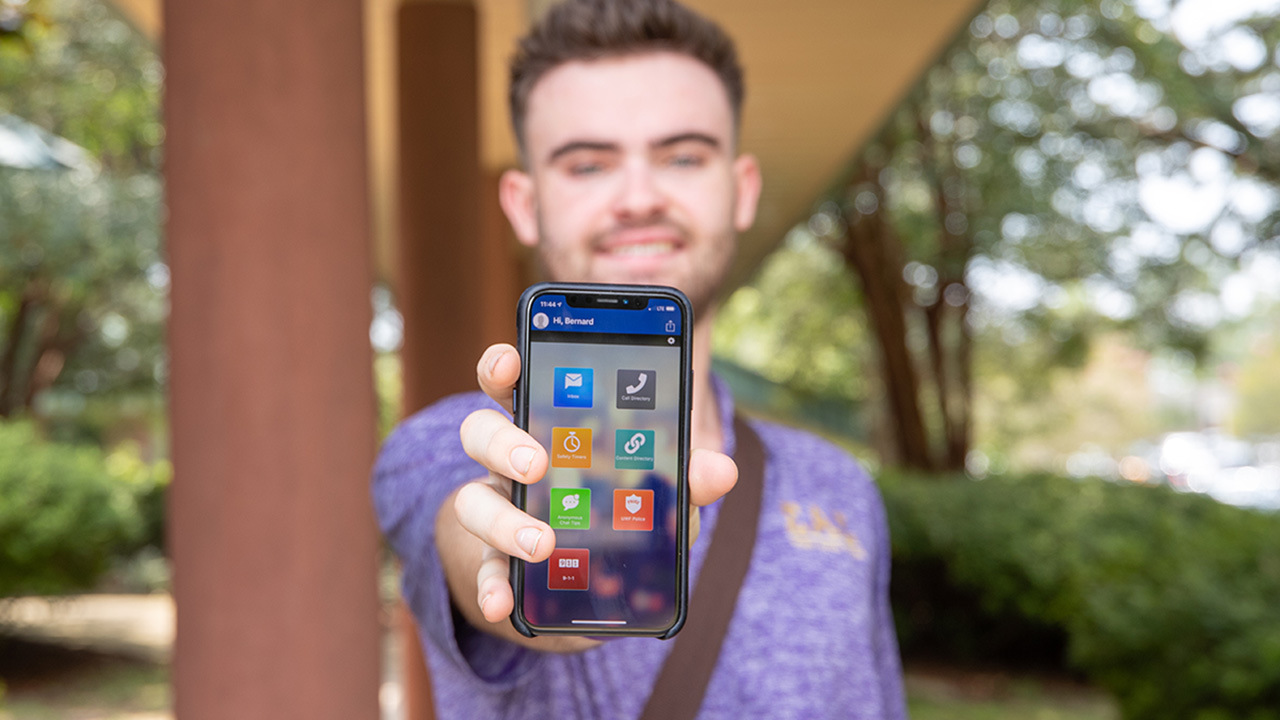 Student holding a mobile phone pointing at the camera with the UWF Gaudian app displayed on the screen.