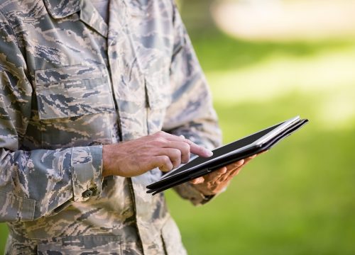 Mid-section of soldier using digital tablet in park on a sunny day