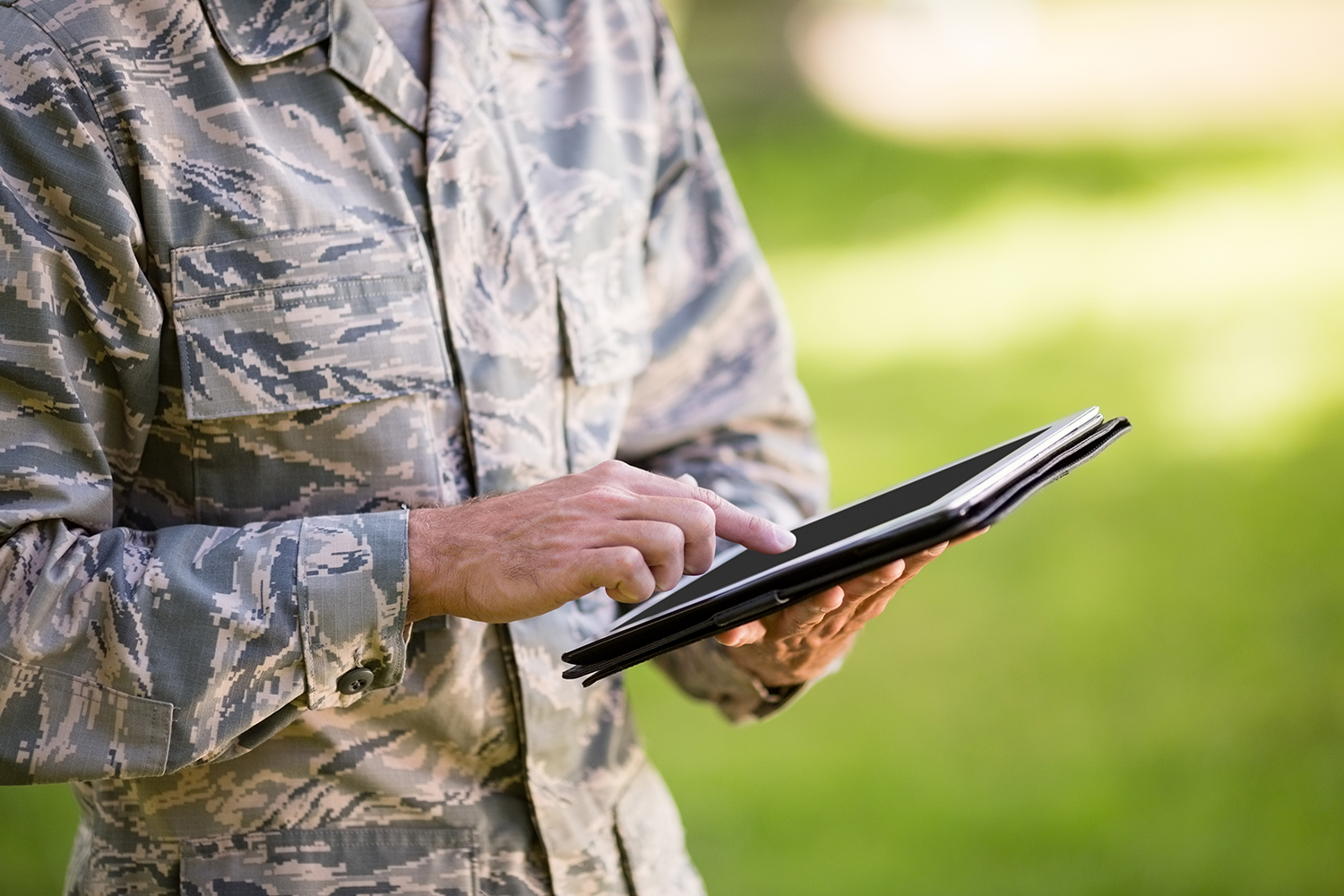 Mid-section of soldier using digital tablet in park on a sunny day