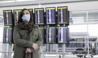 A cautious female traveler at the airport wearing a mask to protect herself from disease, possibly fearful of Ebola.