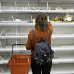 Young woman standing in front of empty shelf in a supermarket