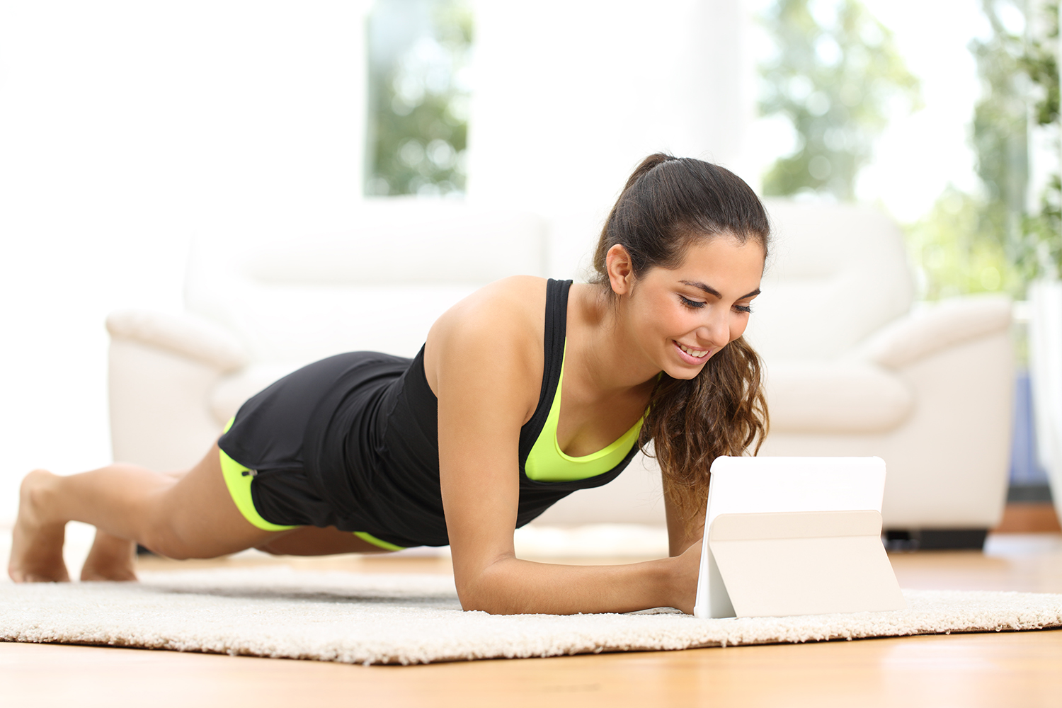 Fitness woman exercising on the floor at home and watching fitness videos in a tablet