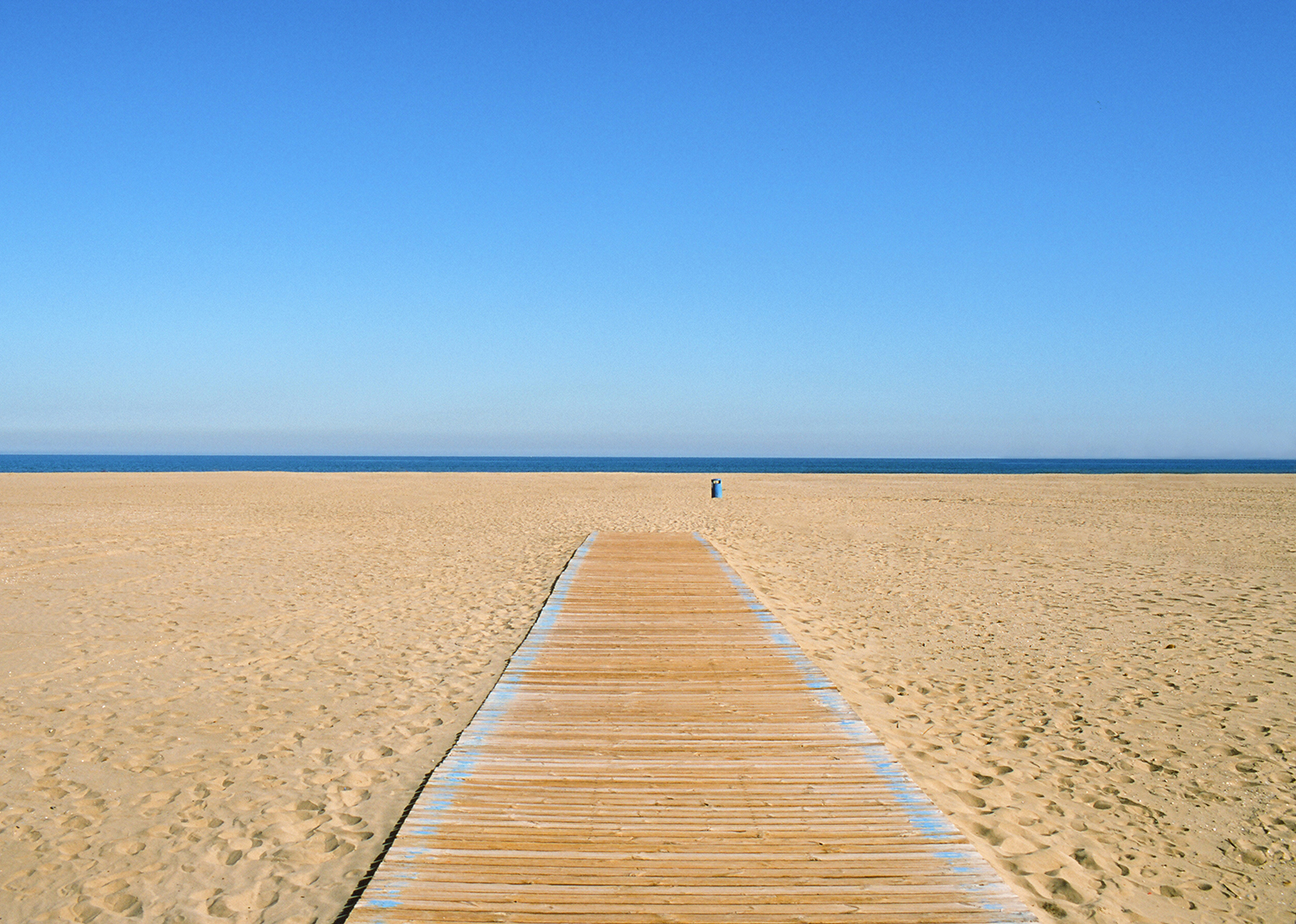 Scene of sea, sky and empty beach with soft sand, wooden pathway and waste container