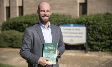 Dr. Jamin Wells, assistant professor and director of the Public History Master’s Program, poses with his recent book, Shipwrecked: Coastal Disasters and the Making of the American Beach, at the College of Arts, Social Sciences and Humanities offices on Nov. 24, 2020.