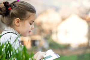 Photo of little girl reading a book outside. Stock photo.