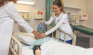 Two nursing students practicing respiratory therapy work in a hospital simulation lab setting.