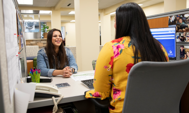 student sits at a desk smiling at an adviser