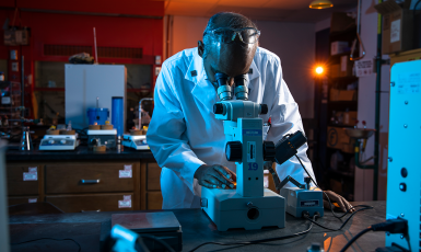 Scientist looks down into a microscope in a lab setting.