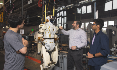 Three people look at a life-size robot in a lab