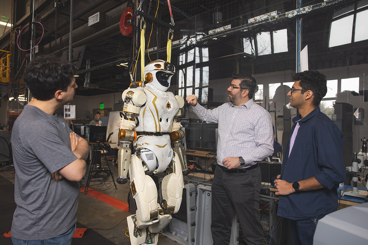 Three people look at a life-size robot in a lab