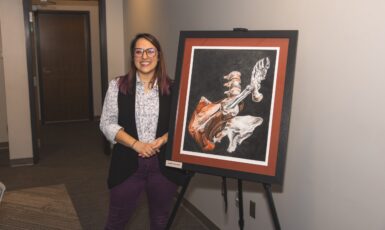 Person stands smiling next to anatomical artwork on an easel.