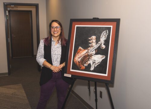 Person stands smiling next to anatomical artwork on an easel.