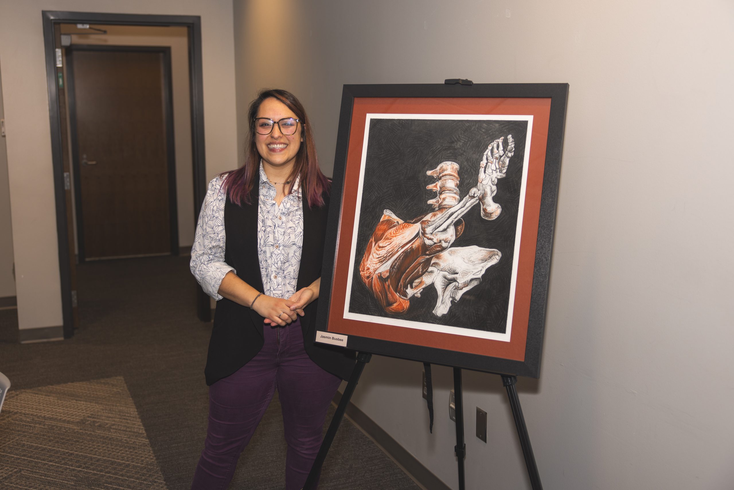 Person stands smiling next to anatomical artwork on an easel.