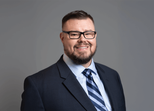 Photo of David Bryant from the shoulders up smiling in a suit and glasses.