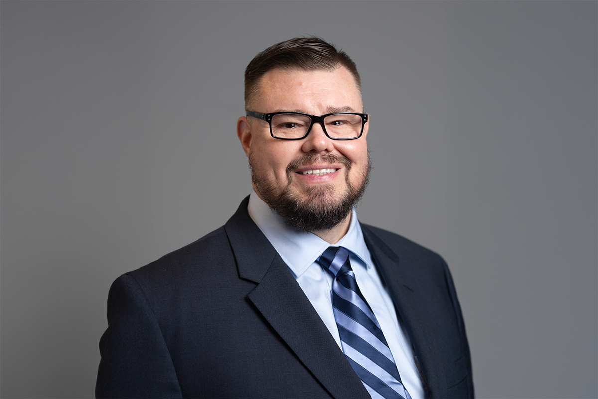 Photo of David Bryant from the shoulders up smiling in a suit and glasses.