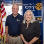 Kevin Green and Dr. Martha D. Saunders pose in front of an American flag and a banner that reads, "Pensacola, FL Rotary Club."
