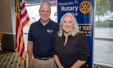 Kevin Green and Dr. Martha D. Saunders pose in front of an American flag and a banner that reads, "Pensacola, FL Rotary Club."