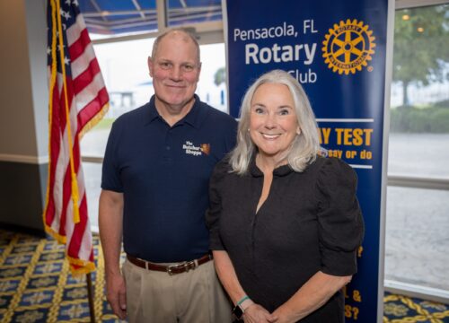 Kevin Green and Dr. Martha D. Saunders pose in front of an American flag and a banner that reads, "Pensacola, FL Rotary Club."