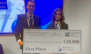 Two students hold a large check that reads, "2025 Southeastern Hedge Fund Competition. Georgia State University, J. Mack Robinson College of Business. Southeastern Alternative Funds Association. Pay to the order of: Alexander Francis, Lorenzo Weber. $10,000. First Place. University of West Florida.