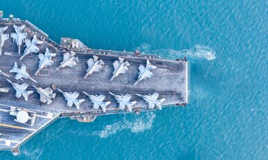 Aerial view of a naval aircraft carrier with aircraft on top of it in blue ocean waters.