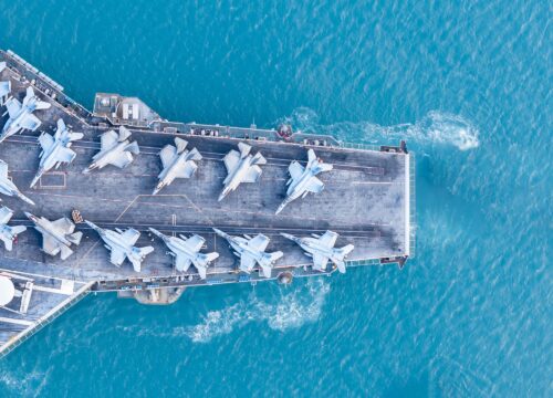 Aerial view of a naval aircraft carrier with aircraft on top of it in blue ocean waters.