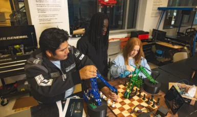 Three students around a robot and chess board in an engineering lab.