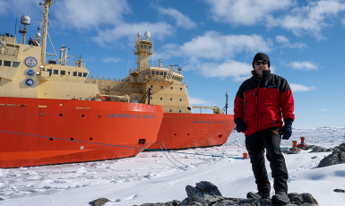 Dr. Wade Jeffrey stands on rocks and ice in front of two ships named Laurence M. Gould and Nathaniel B. Palmer.