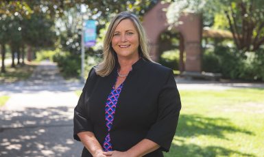 Dr. Mary Anderson stands smiling in front of the UWF archway and blue and purple banner.