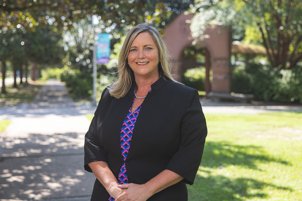 Dr. Mary Anderson stands smiling in front of the UWF archway and blue and purple banner.