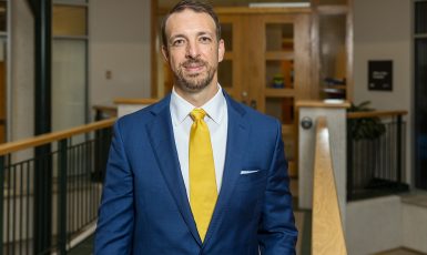 Clifford Humphrey stands in front of a wooden door with windows next to a wooden railing.