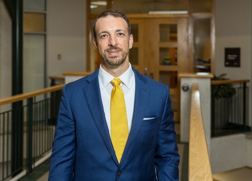Clifford Humphrey stands in front of a wooden door with windows next to a wooden railing.