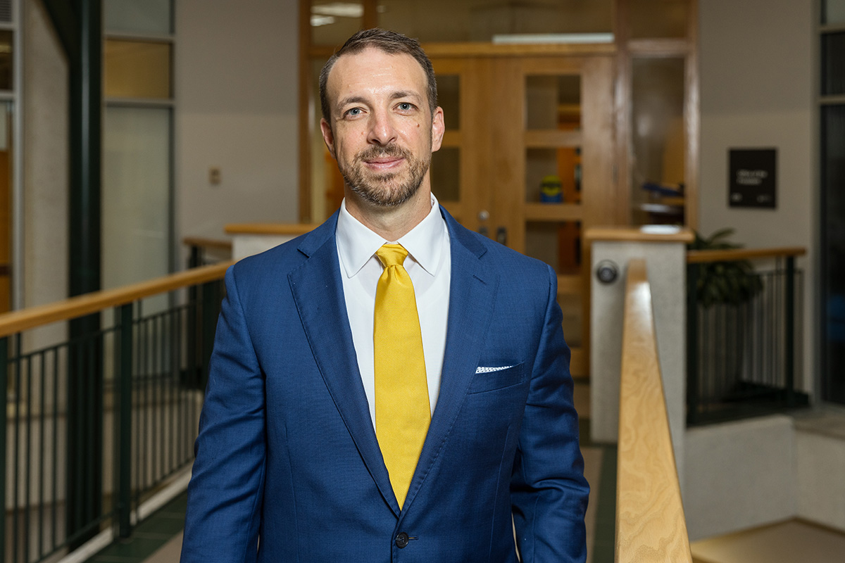 Clifford Humphrey stands in front of a wooden door with windows next to a wooden railing.