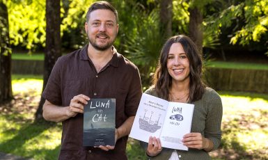 Two people stand side by side smiling. One holds a book showing the cover that says, "Luna the Cat" and the other holds a book open to pages.