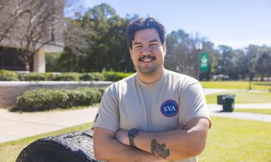 UWF student veteran stands with arms crossed smiling in front of the cannon on the UWF Cannon Green