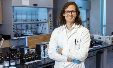 Photo: Person in a white lab coat stands with arms crossed in a chemistry lab.