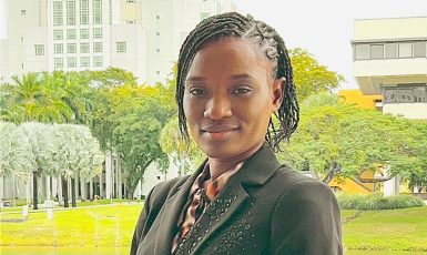 Photo: UWF student Lousindy Mitton soft smiles with green trees and grass in the background.