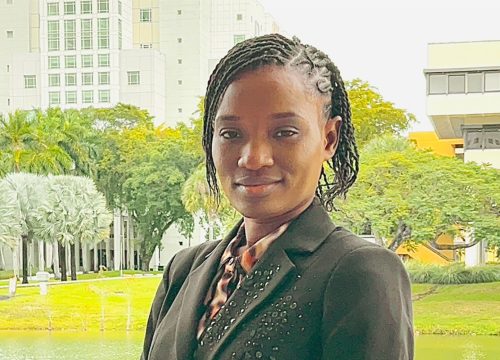 Photo: UWF student Lousindy Mitton soft smiles with green trees and grass in the background.