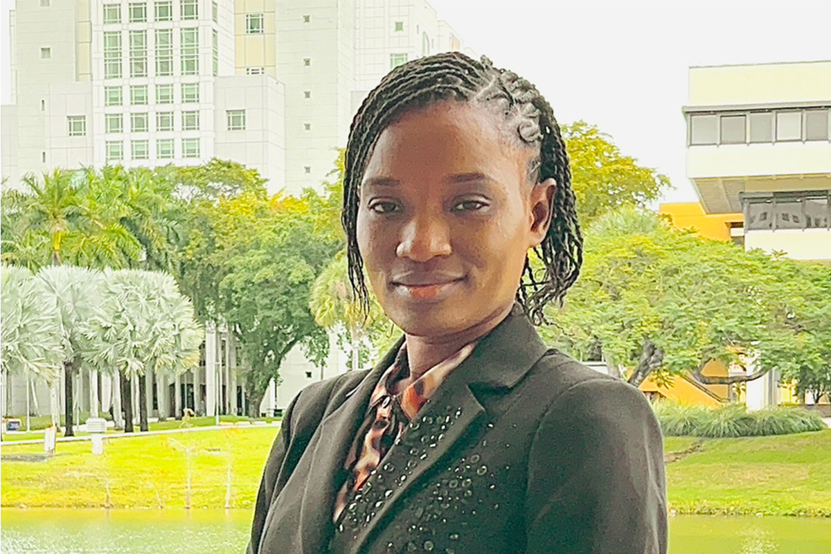 Photo: UWF student Lousindy Mitton soft smiles with green trees and grass in the background.