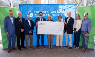 Photo: Nine people stand in front of a blue backdrop that reads, "University of West Florida Lewis Bear Jr. College of Business" with a green nautilus shell backdrop on both sides. The three people in the center hold a large check with text: "Warren Averett. Date: September 19, 2025. Pay to the order of University of West Florida $250,000 Two Hundred & Fifty Thousand 00/100 dollars. Memo: Lifetime Giving Lewis Bear Jr. College of Business." Signed, "Warren Averett."