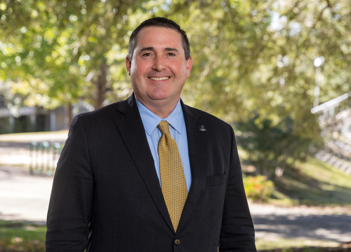 UWF's Dan Lucas smiles in front of greenery on campus.