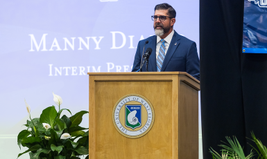 President Manny Diaz Jr. gives a speech behind a podium. Screen behind him reads, "Manny Diaz Jr. Interim President."