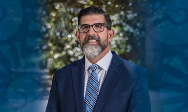 Dark blue nautilus shell graphic on both sides of a headshot of UWF Interim President Many Diaz Jr.