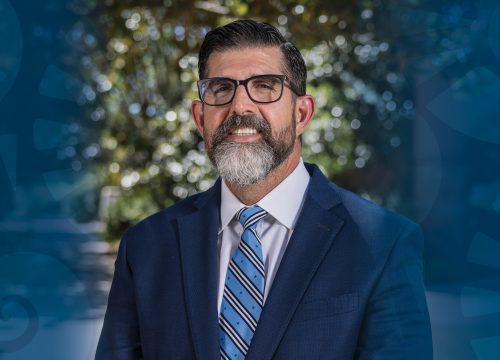 Dark blue nautilus shell graphic on both sides of a headshot of UWF Interim President Many Diaz Jr.