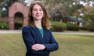 Student stands with arms crossed in front of archway.